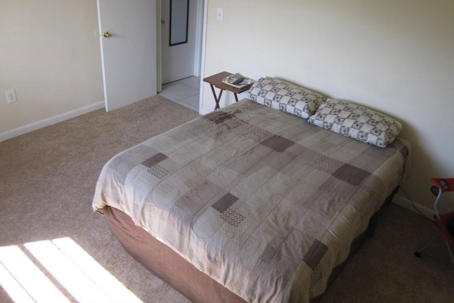A full sized bed sits next to a small side table in the middle of a room in the three-bedroom rental.