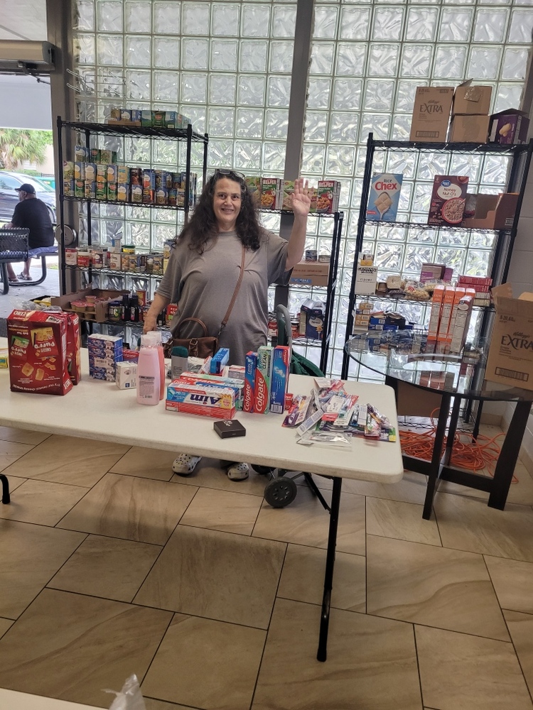 Lady surrounded by various items the food pantry has available.