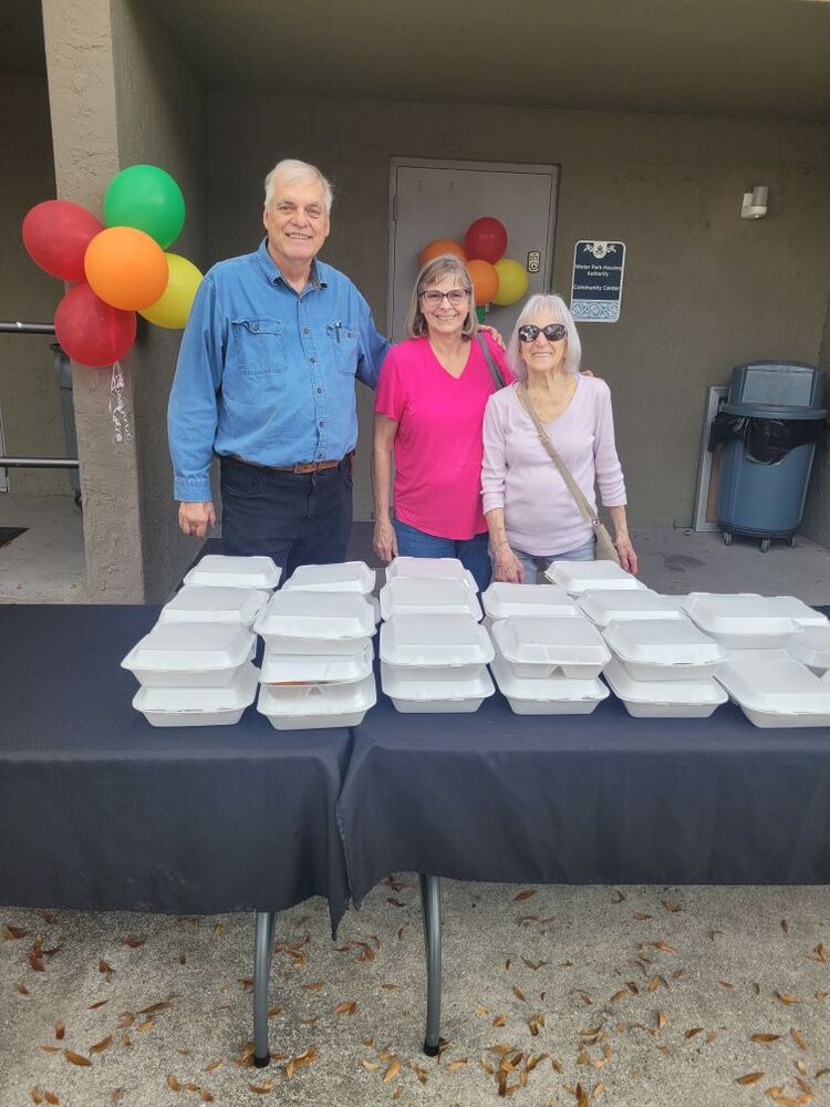 Three people standing behind a table with to go lunch containers.