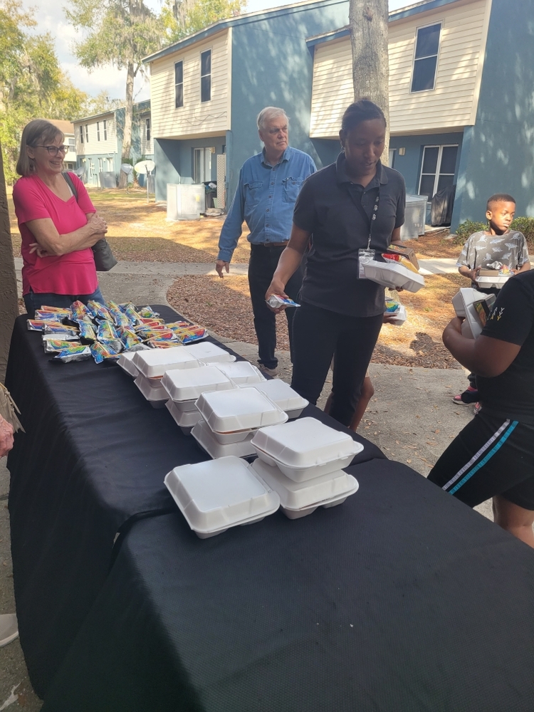 Three people standing behind a table with to go lunch containers.