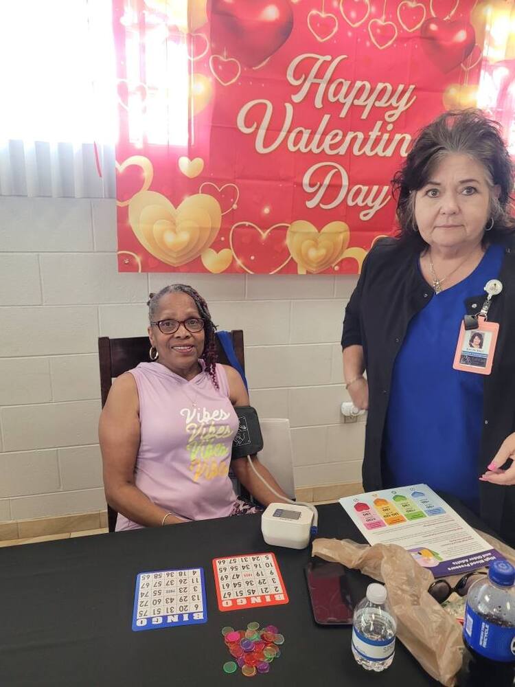 Two ladies behind a table, one taking the others blood pressure.